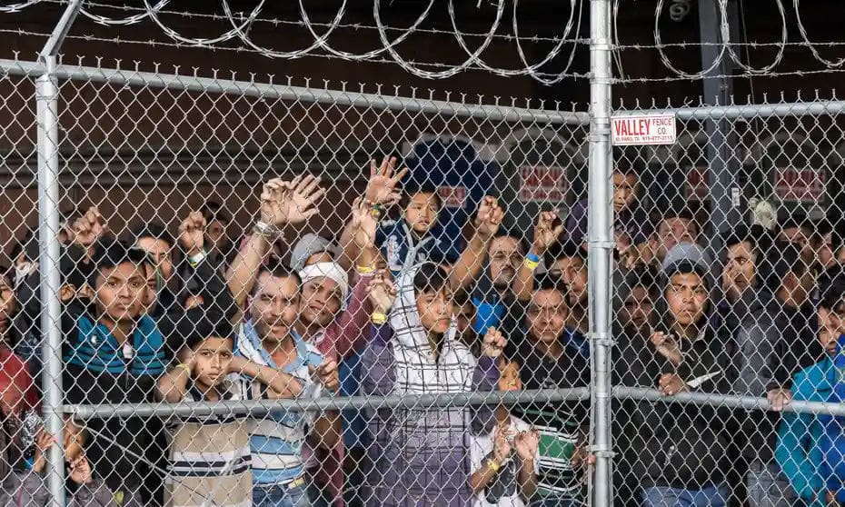 Mexican immigrants, adults and kids, are standing next to the metal fence